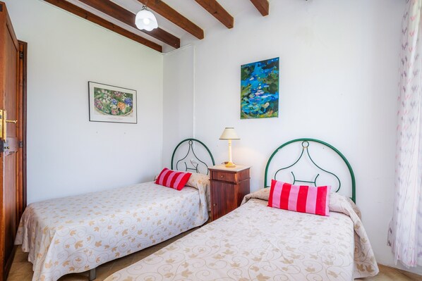 Una habitación con dos camas, una puerta de madera, un cuadro y una lámpara.