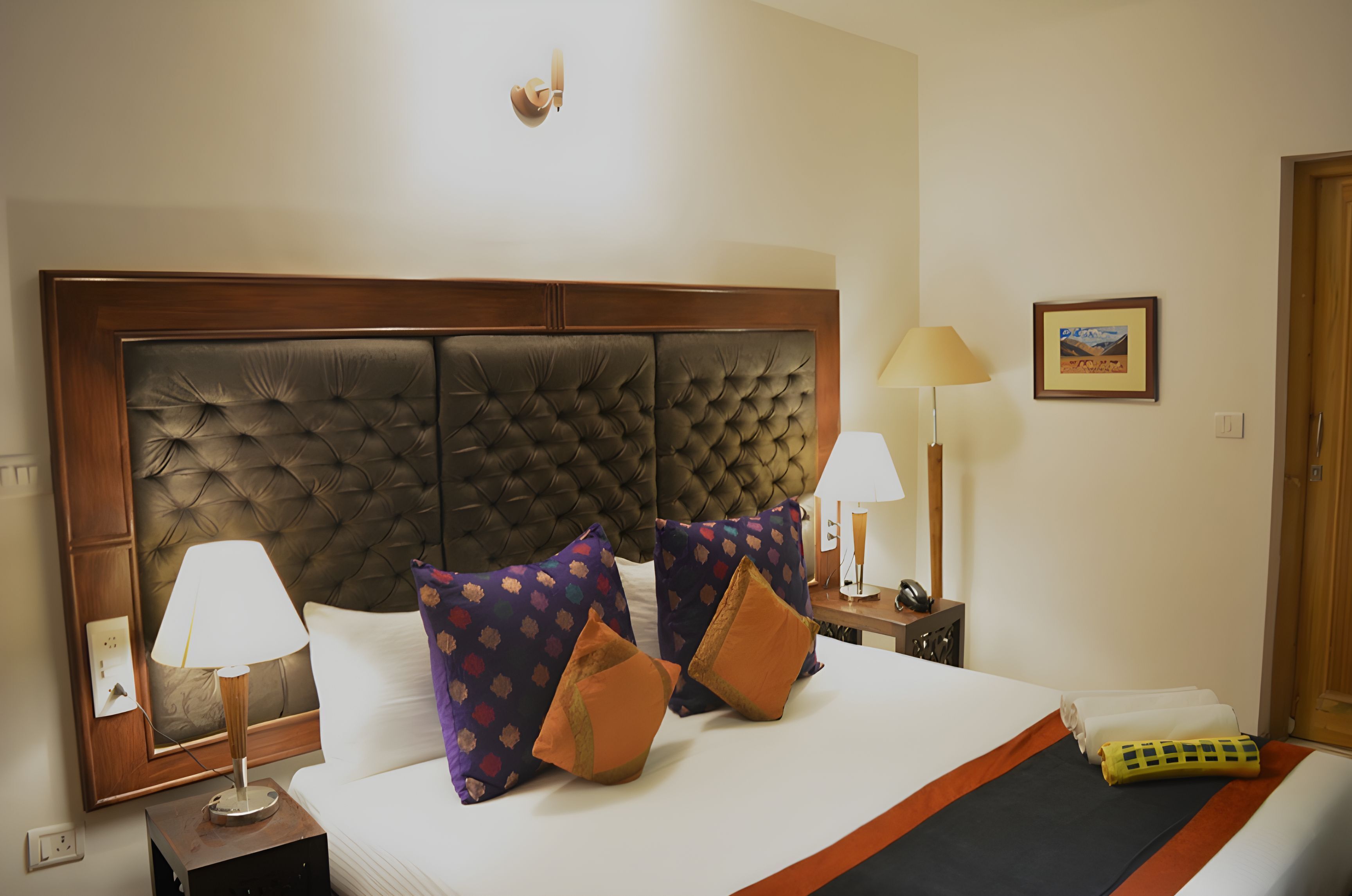 A hotel room with a large bed, two bedside lamps, a framed picture on the wall, and a wooden door.