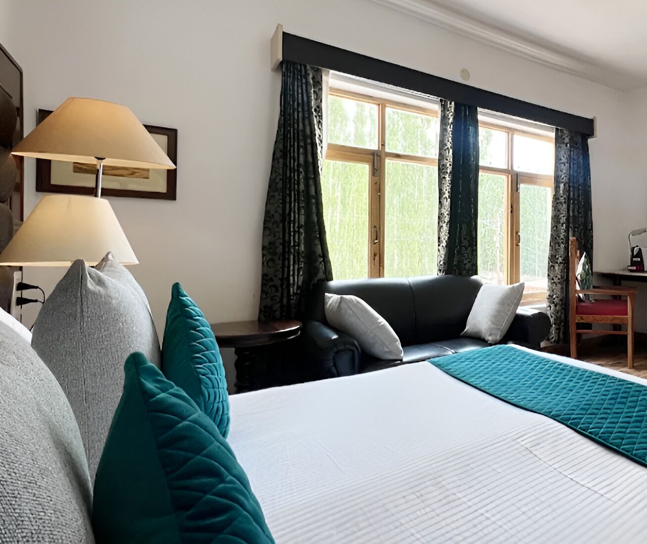 A hotel room with a large bed, two bedside tables, a desk, a chair, and a window with curtains.