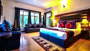 A hotel room with a large bed, a sofa, a small table, and a window with curtains. - Gomang Boutique Hotel  (Leh)
