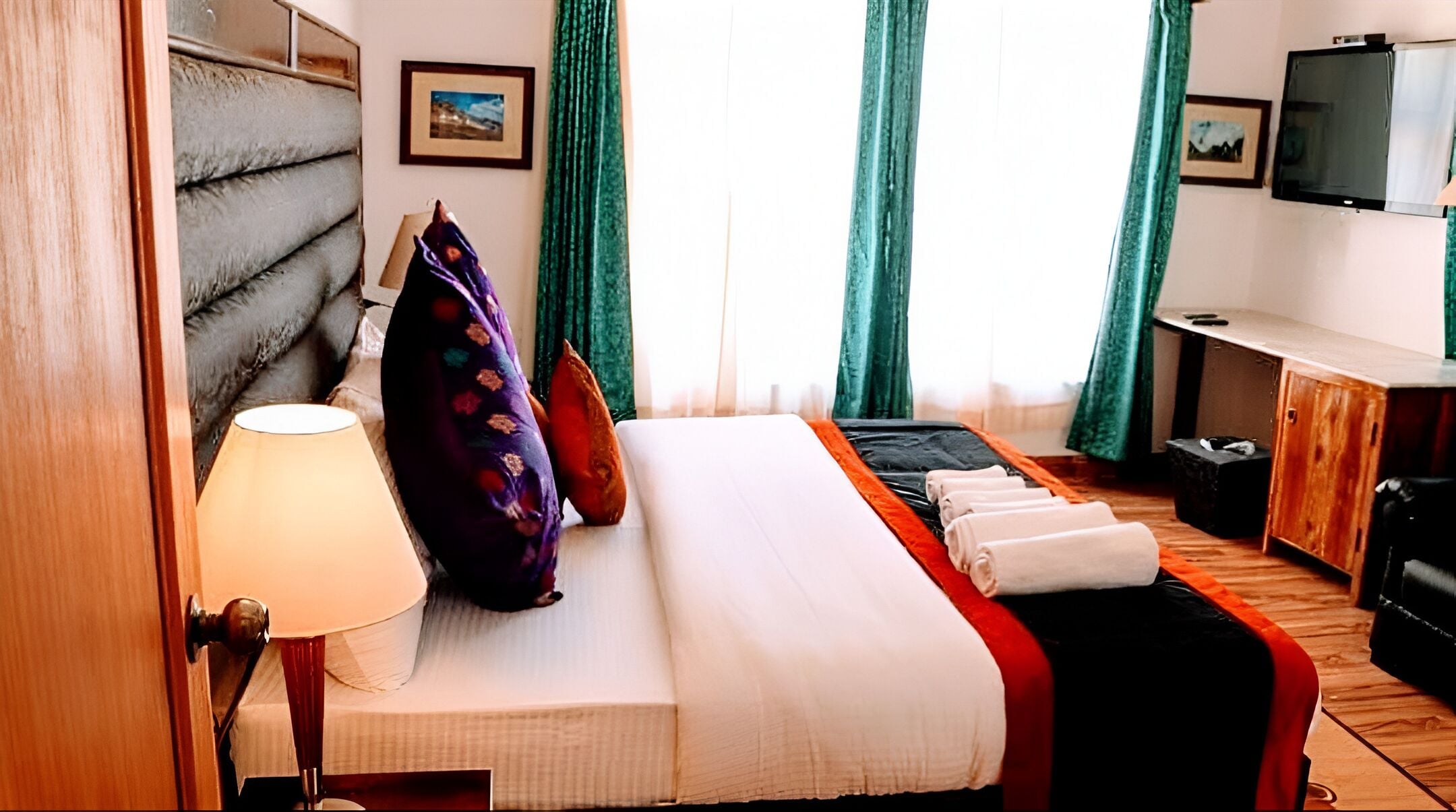 Una habitación de hotel con cama, escritorio, televisor y ventana con cortinas.