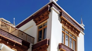 A building with a white facade, large windows, and wooden balconies. There are outdoor seating areas with orange chairs and white umbrellas. - Gomang Boutique Hotel  (Leh)