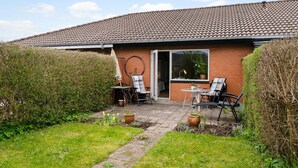 A brick house with a tiled roof, a patio with outdoor furniture, and a garden area.