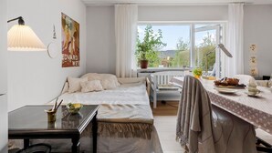 A cozy room with a bed, a table with a lamp, a window with curtains, and a poster on the wall.