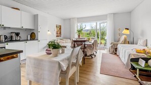 A bright, open-plan living space with a kitchen, dining area, and a large window offering a view of the outdoors.
