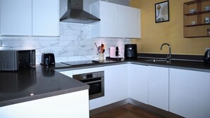 A modern kitchen with white cabinets, a stainless steel range hood, a microwave, a coffee maker, and a sink.