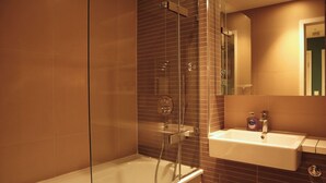 A modern bathroom with a glass-enclosed shower, a white bathtub, and a sink with a mirror above it.