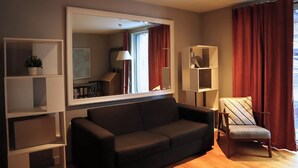 A living room with a black sofa, a chair, a large mirror, and a bookshelf.