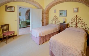 Ein Schlafzimmer mit zwei Betten, einem Sessel und einem kleinen Tisch. Eine Tür führt in einen anderen Raum.