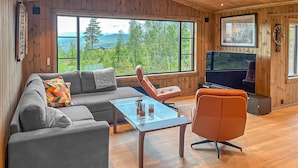 A cozy living room with a sofa, armchair, and coffee table, large windows with a scenic view, and a flat-screen TV. - 2 bedroom awesome home in Engerdal (Engerdal)