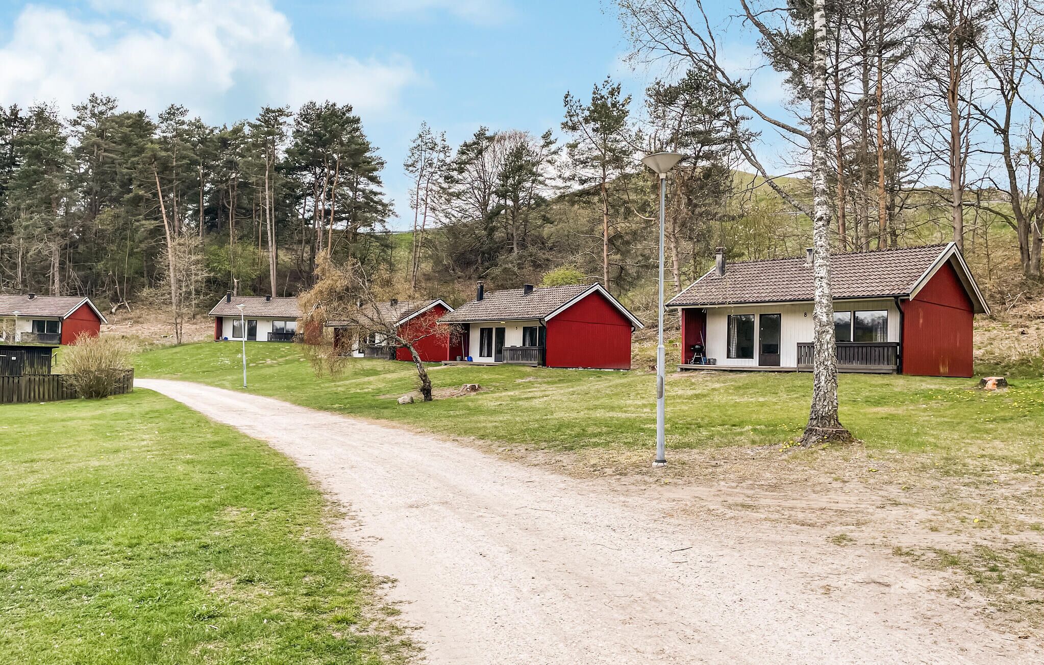 A row of red cabins with a dirt path leading to them, surrounded by trees and a grassy area.