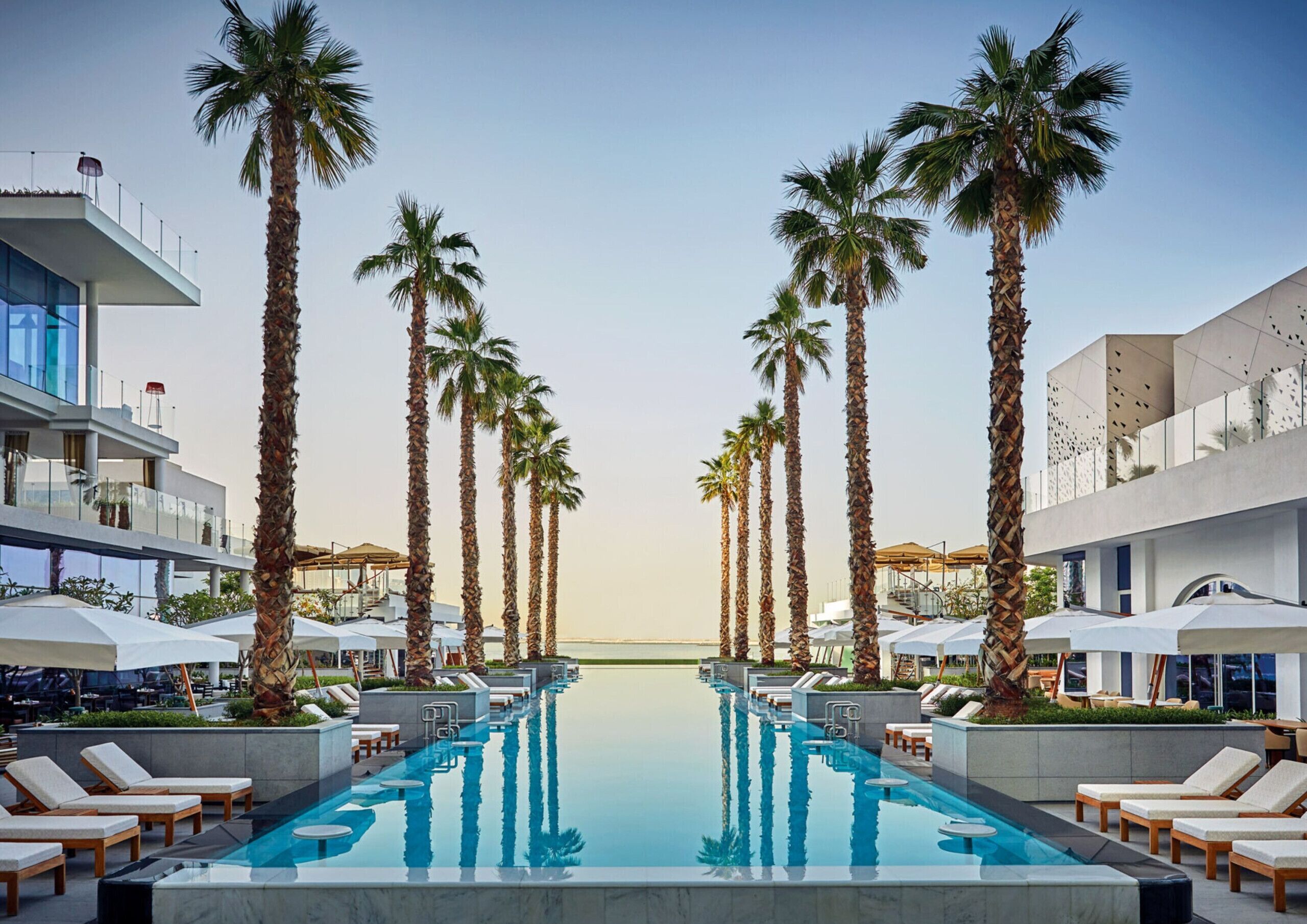 A poolside area with lounge chairs, palm trees, and modern buildings.