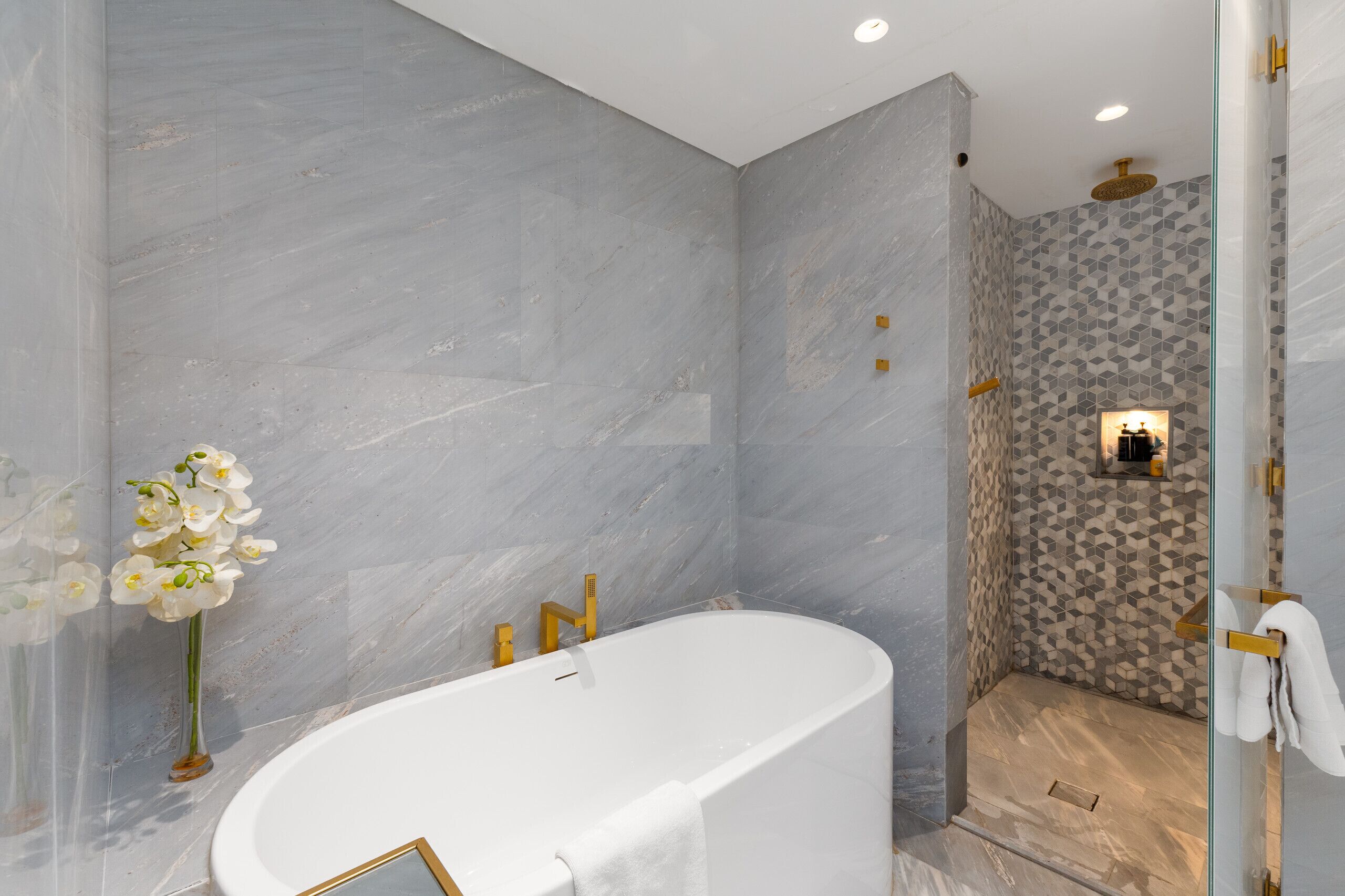 A modern bathroom with a freestanding bathtub, a shower area with a geometric tile pattern, and a vase of white orchids.