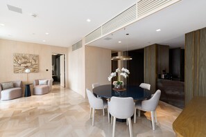 A modern dining area with a round table, six chairs, and a vase of white flowers.