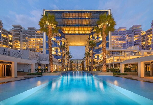 A modern hotel with a central pool, multiple floors, and palm trees.