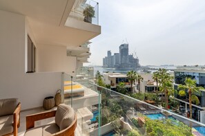 Un apartamento moderno con balcón de vidrio que da a una piscina y un paisaje urbano.