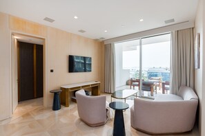 En moderne stue med et fladskærms-tv, to sofaer, et glasbord og en stor skydedør, der fører ud til en balkon.