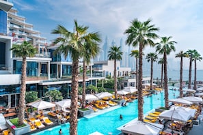 A rooftop pool area with multiple levels of balconies, palm trees, and a view of the city skyline.