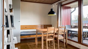 Ein kompakter Raum mit einer hölzernen Sitzbank, einem Tisch und Stühlen. Eine schwarze Pendelleuchte hängt von der Decke.