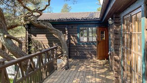 A wooden cabin with a wooden deck, a large tree in front, and a garage with a door.