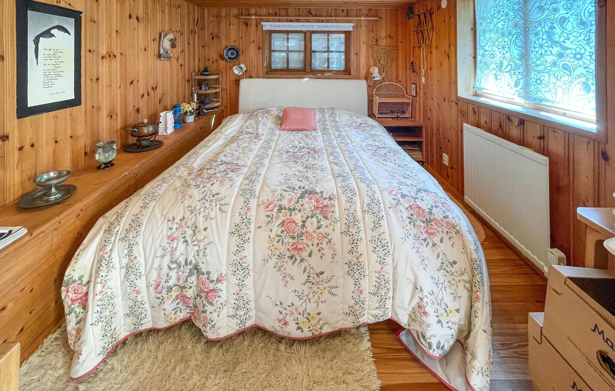 A cozy wooden room with a bed, a window with patterned curtains, and a shelf with various items.