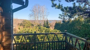 A wooden deck with a railing overlooking a forested area and a body of water in the distance.