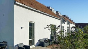 Een modern huis met twee verdiepingen, een witte gevel, een bruin pannendak en een klein terras met tuinmeubilair.