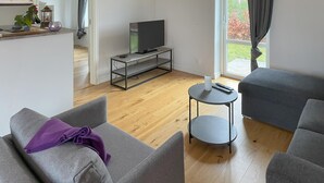 Een moderne woonkamer met grijze banken, een klein rond tafeltje en een tv op een metalen standaard.