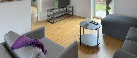A modern living room with grey sofas, a small round table, and a TV on a metal stand.