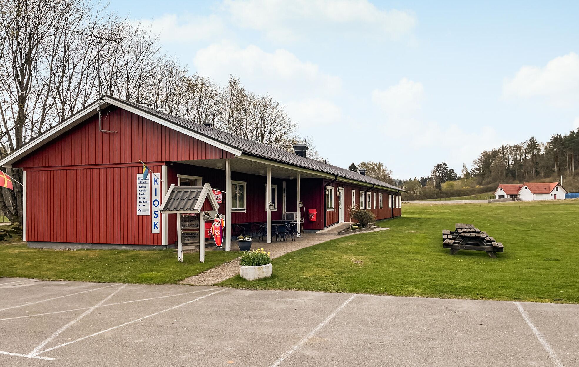 A red building with a covered porch, a signboard listing amenities, and a parking area.