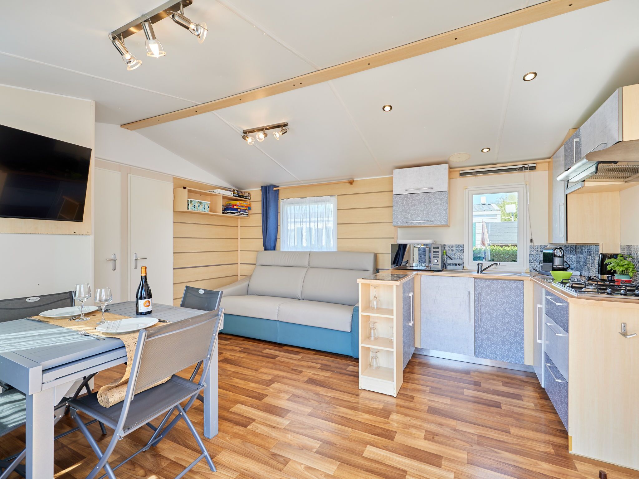 A compact kitchenette with a stove, microwave, and sink. There is a dining area with a table and chairs, and a sofa with a window.