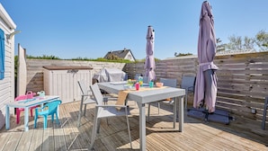An outdoor deck with a table and chairs, a barbecue grill, and umbrellas. - Super Octalia (camping 5*) by Interhome (Les Pieux)