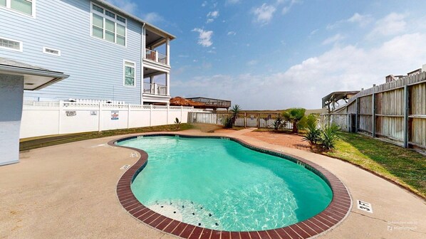 A swimming pool with a brick border, surrounded by a fenced yard with a building and a wooden deck. - Shared Pool, Close to the Beach, Studio Condo (Corpus Christi)