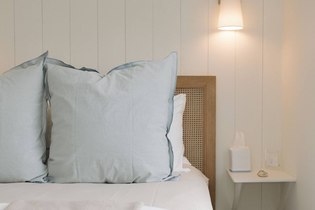A neatly made bed with two pillows, a bedside table with a tissue box, and a wall-mounted lamp.
