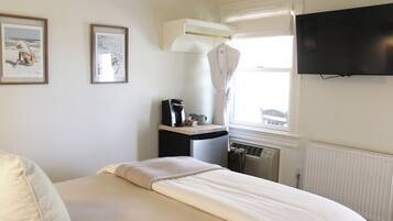 A bedroom with a bed, a desk with a coffee maker, a radiator, and a TV on the wall.