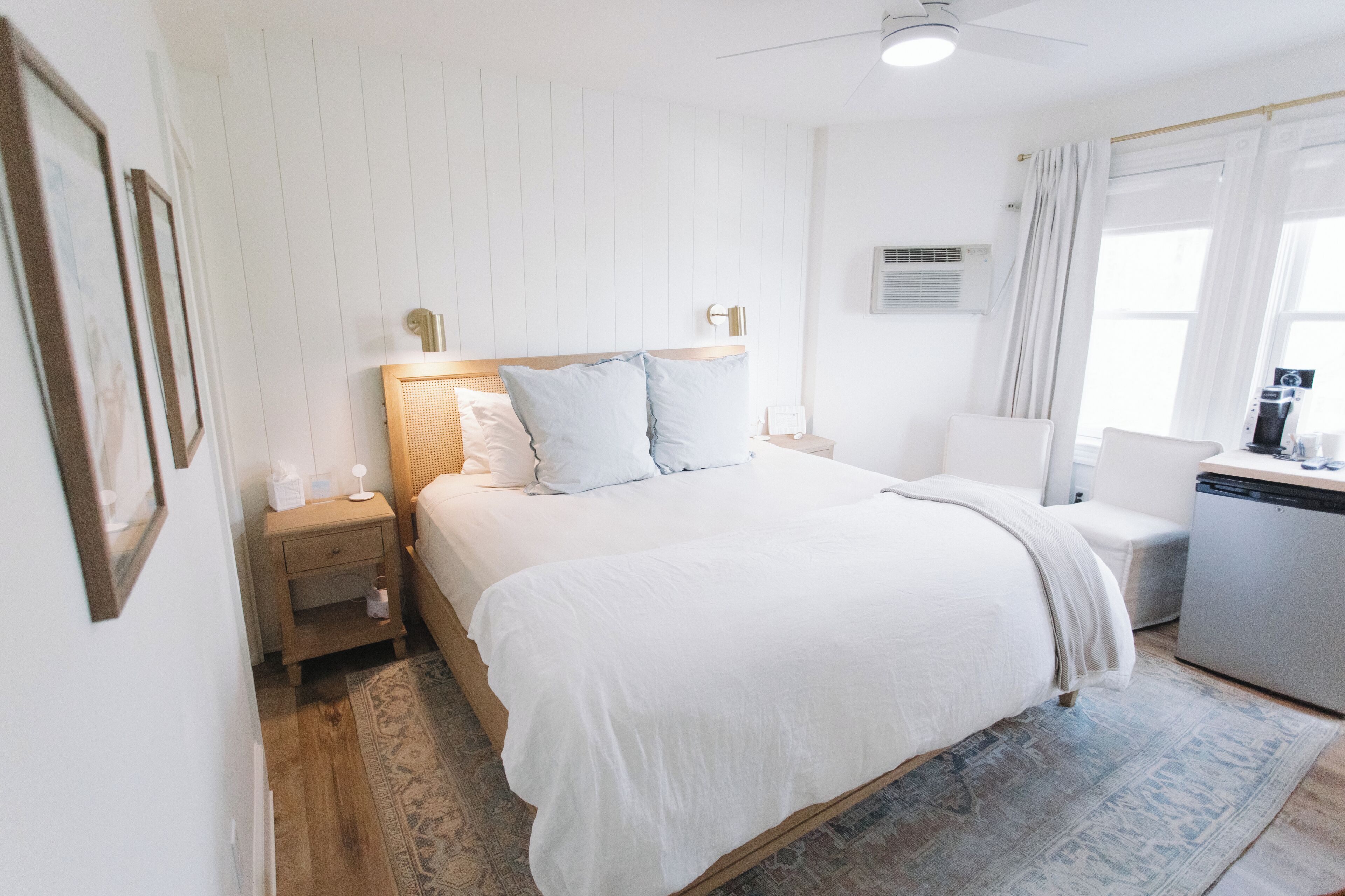 A bedroom with a bed, a nightstand, a bedside table, a wall-mounted air conditioner, and a window with curtains.
