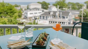 A table set with a martini glass, a cocktail with an orange garnish, a pitcher of water, and a dish of food. - The Trident Inn (Ogunquit)
