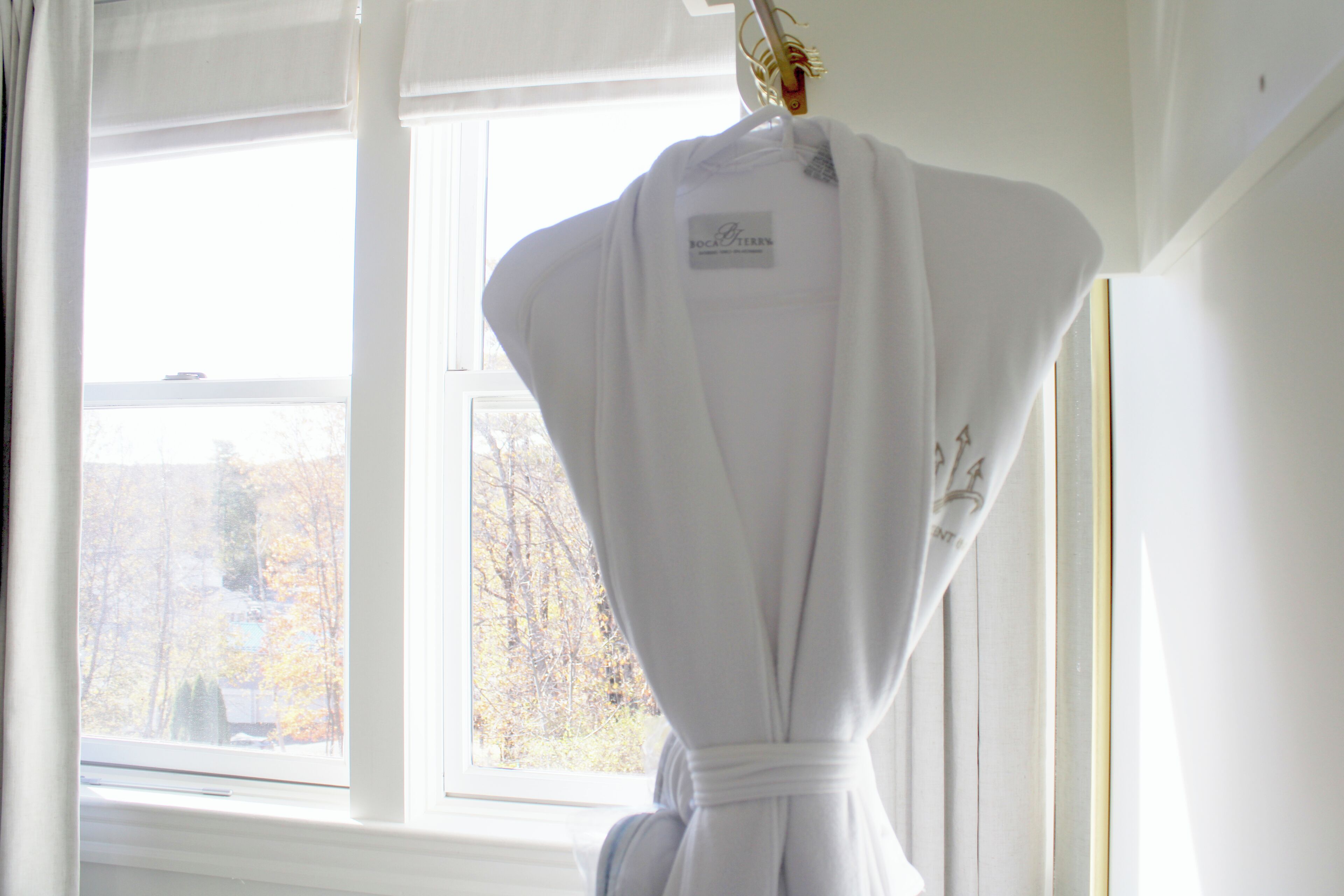A white robe hanging by a window with a view of trees outside.