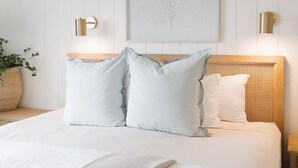 A neatly made bed with two pillows, a woven headboard, and a wall-mounted light fixture. - The Trident Inn (Ogunquit)