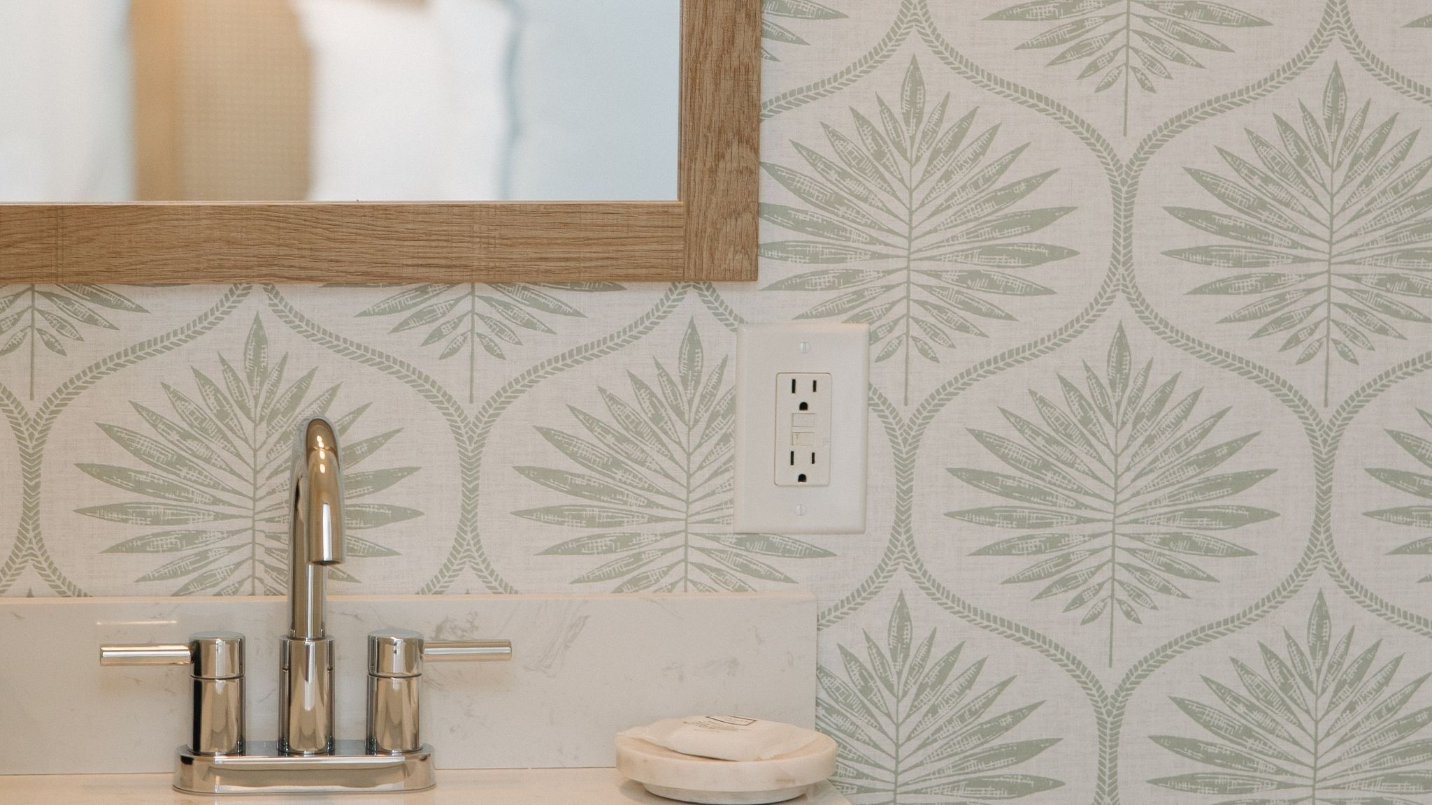 A bathroom with a modern sink, a mirror, and a patterned wallpaper.