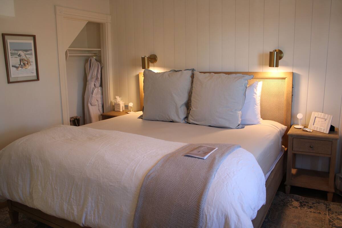 A neatly made bed with a headboard, a bedside table with a lamp, and a nightstand with a framed picture.