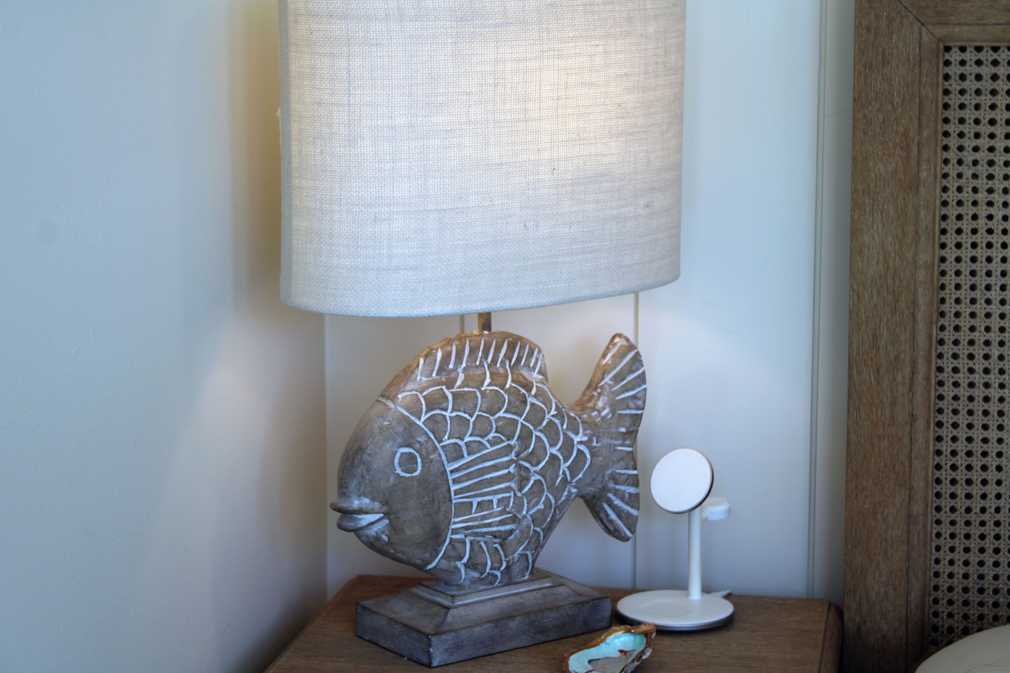 A lamp with a fish-shaped base, a round mirror, and a small blue object on a wooden nightstand.