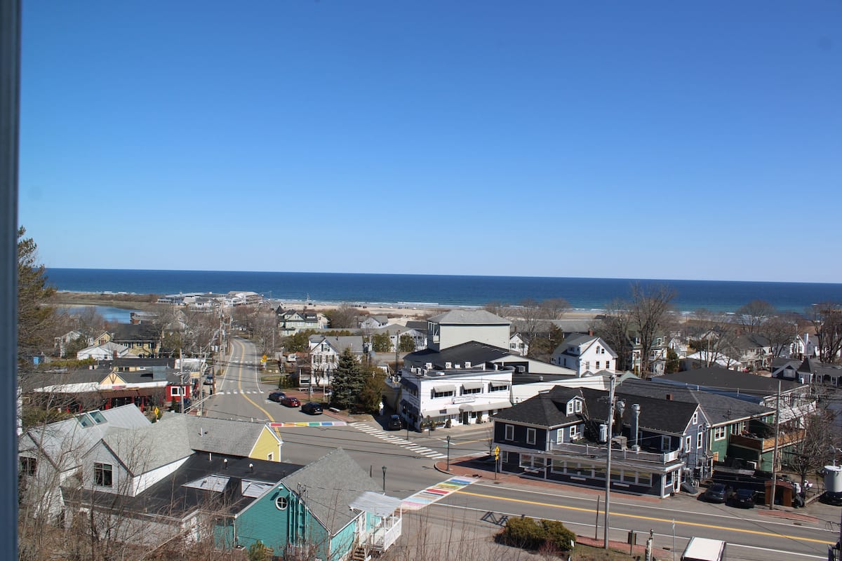 A coastal town with a mix of residential and commercial buildings, a clear sky, and a view of the ocean.