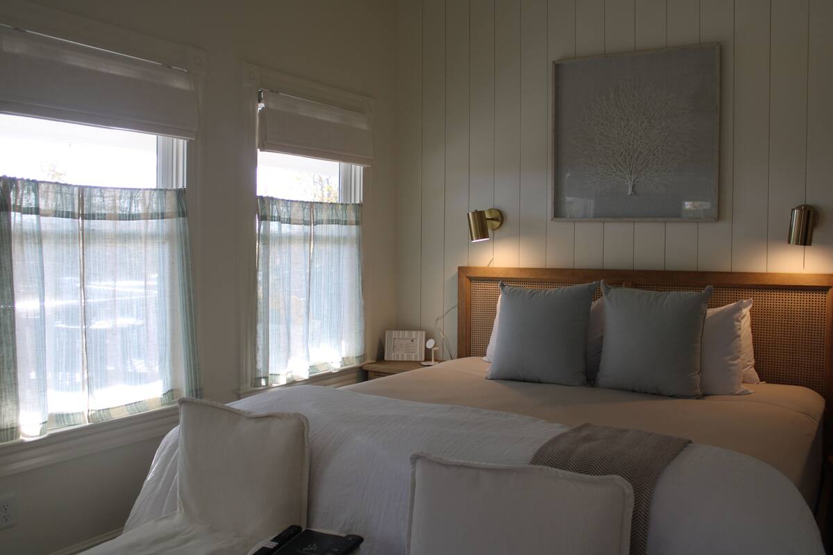 A hotel room with a large bed, a bedside table, a nightstand, a wall-mounted lamp, and a framed picture on the wall.