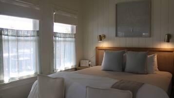 A hotel room with a large bed, a bedside table, a nightstand, a wall-mounted lamp, and a framed picture on the wall.