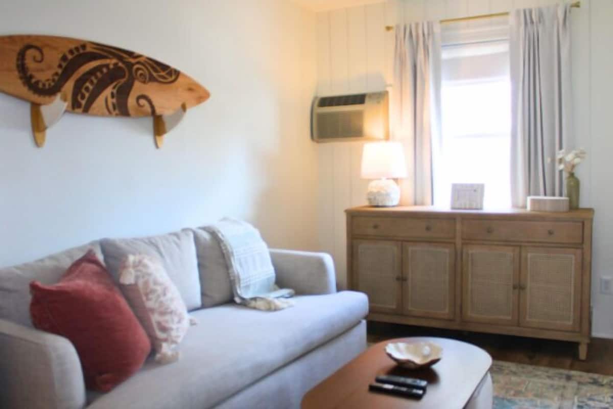 A living room with a sofa, a wooden cabinet, a lamp, and a decorative wall piece.