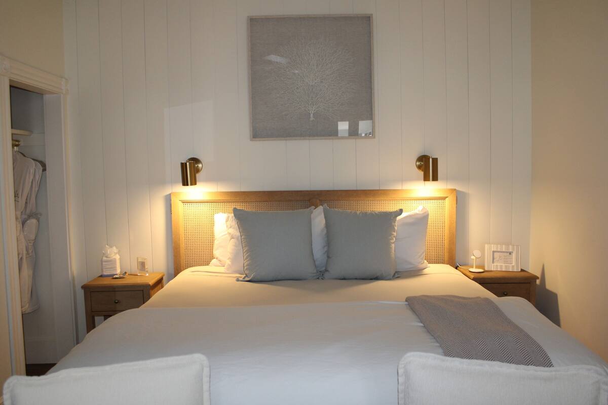 A neatly made bed with pillows, a bedside table with a lamp, and a framed picture on the wall.