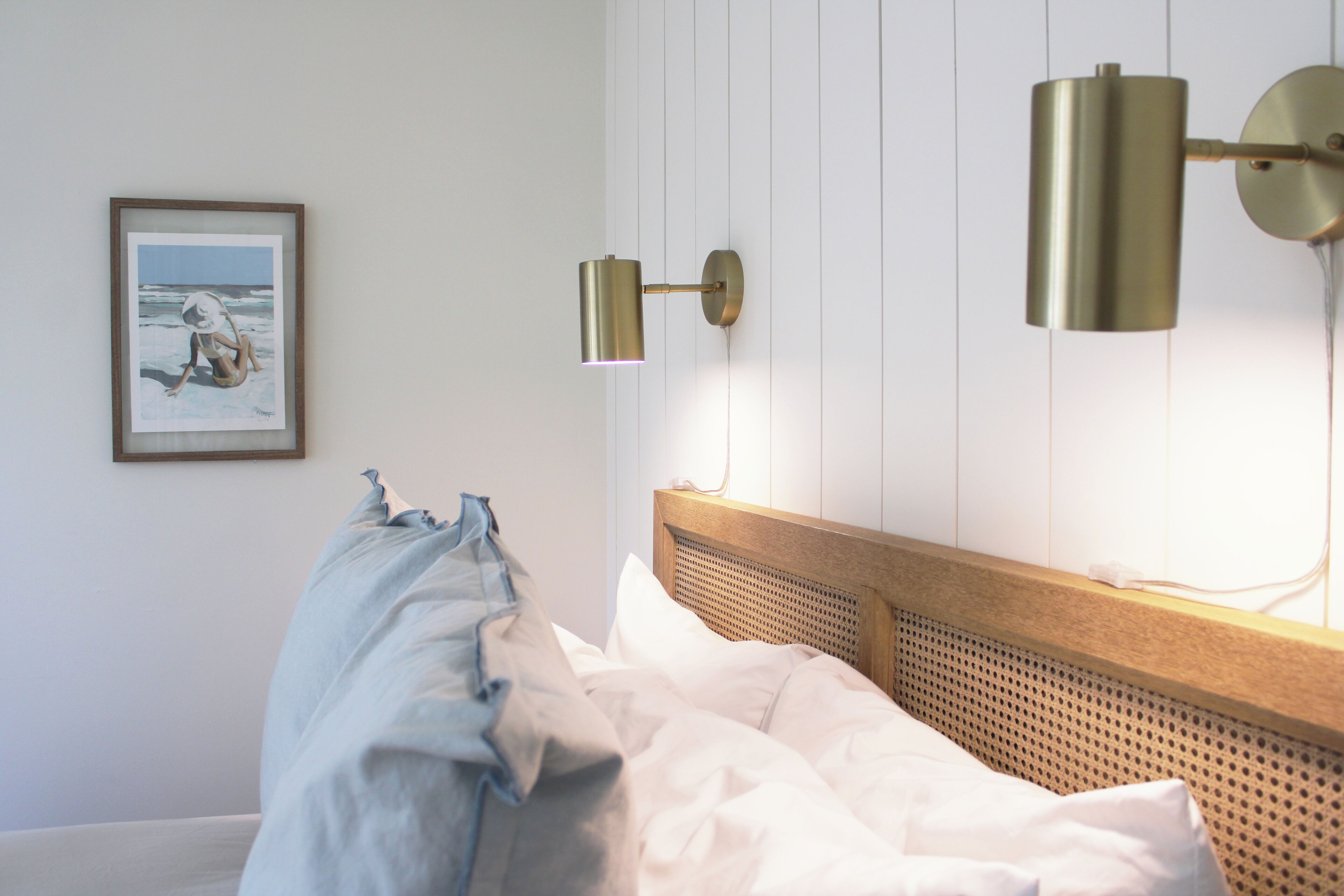 A neatly made bed with white linens, a wooden headboard, and a wall-mounted lamp.
