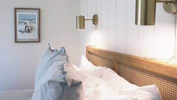 A neatly made bed with white linens, a wooden headboard, and a wall-mounted lamp.