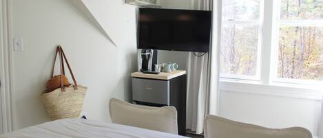 A hotel room with a bed, a desk with a television, a coffee maker, and a window with a view of trees.
